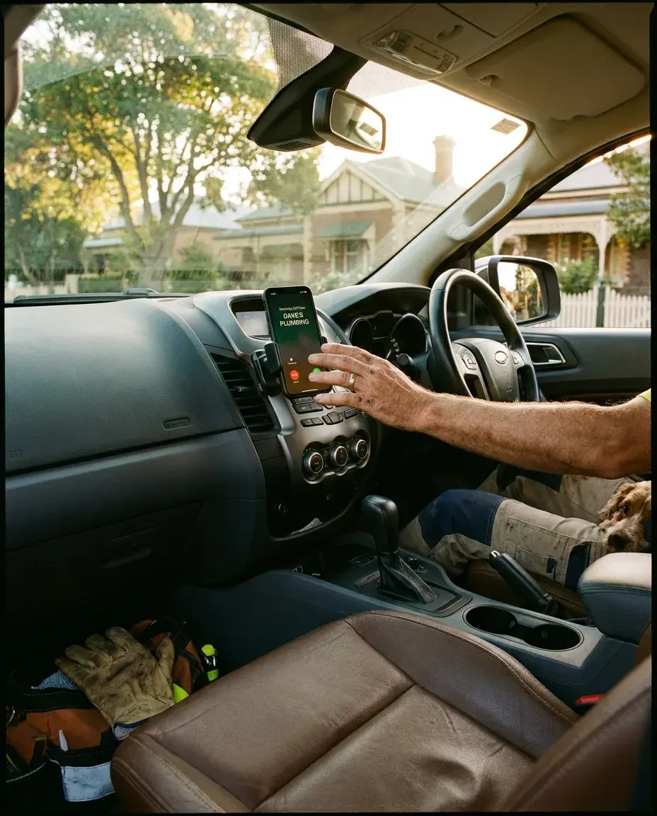 A tradie's hand reaching for a phone lighting up with a call on the dash mount (concept)